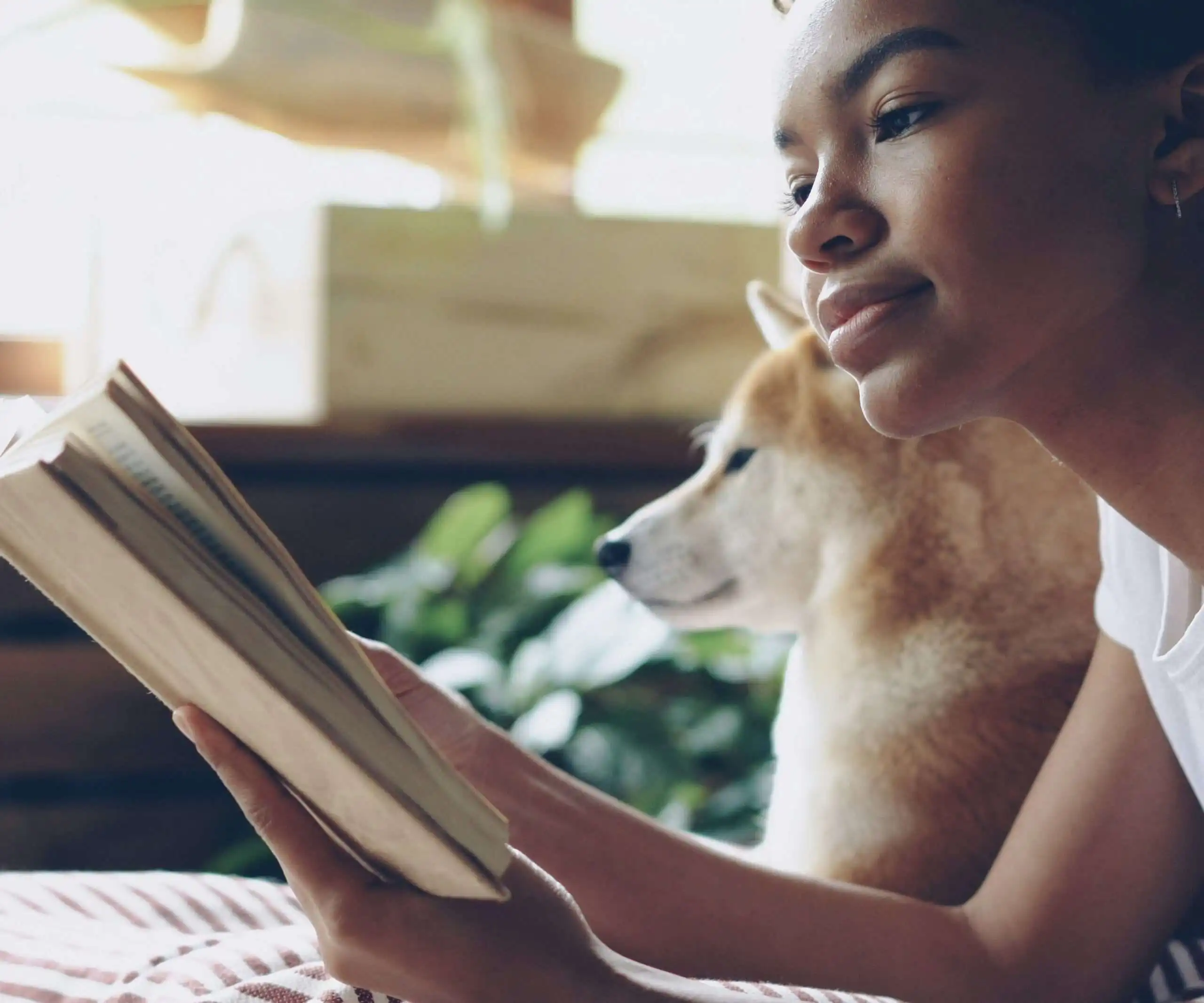 A woman and her dog reading a book about dogs together, cozily, on the bed together.